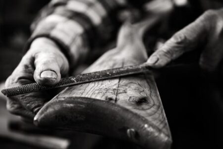 Elderly craftsman filing wood with a rasp file on a workbench