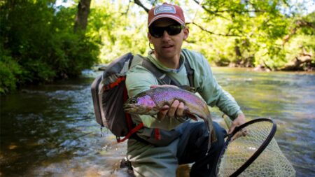 6 Easy-to-Fix Mistakes Beginner Fly Anglers Make While Trout Fishing Man holding a rainbow trout while fly fishing in a clear forest stream.