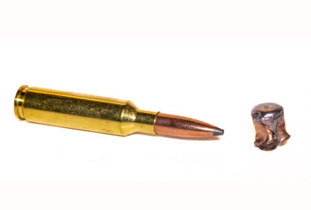 Unfired rifle cartridge beside a deformed expanded bullet on white background