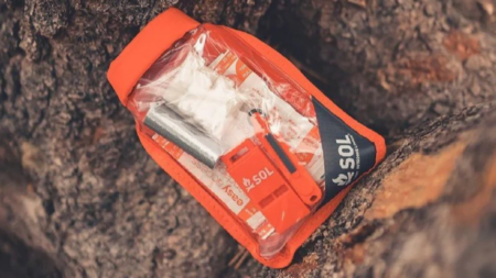 SOL branded orange emergency survival kit resting in tree bark crevice outdoors