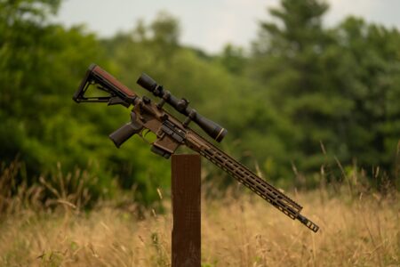 AR-15 rifle with scope displayed on wooden post in outdoor field setting