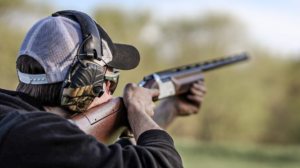 Person wearing ear protection aiming shotgun outdoors during clay pigeon shooting sport