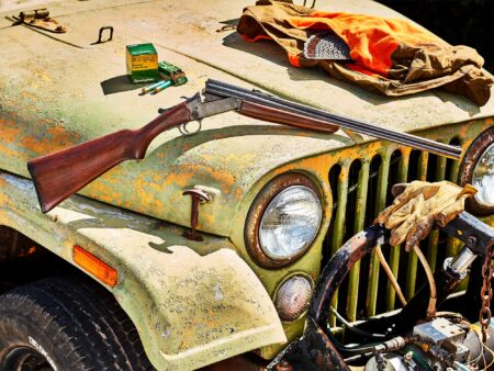 Remington shotgun and ammunition box on rusty vintage Jeep hood with hunting gear