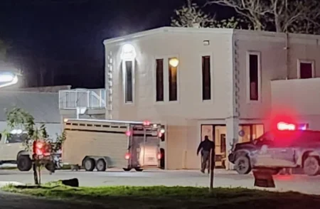 Night scene showing emergency vehicles with flashing lights outside a two-story white building.