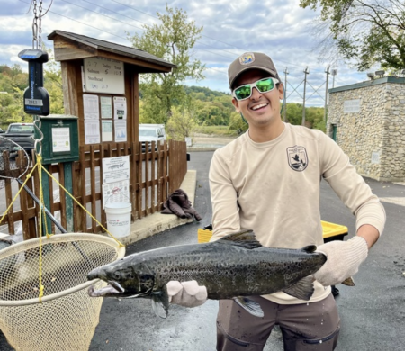 Smiling fisherman holding large caught salmon near fishing weigh station outdoors