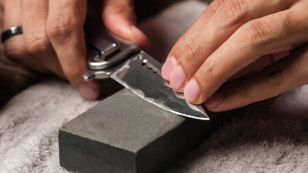 Hands sharpening a folding pocket knife on a gray whetstone