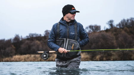 The Best Fishing Waders Man fly fishing in river wearing Simms waders and jacket on overcast day
