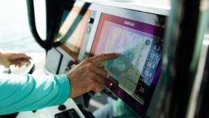 Person pointing at Simrad marine chartplotter navigation screen on a boat