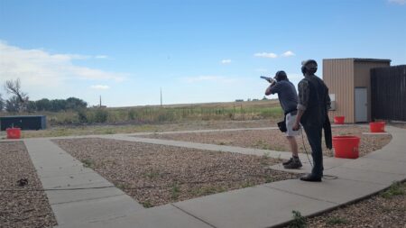 Two people practicing skeet shooting at an outdoor shooting range on a clear day.