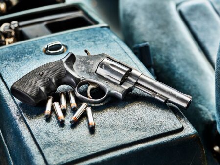 Stainless steel revolver handgun with loose bullets on blue leather surface