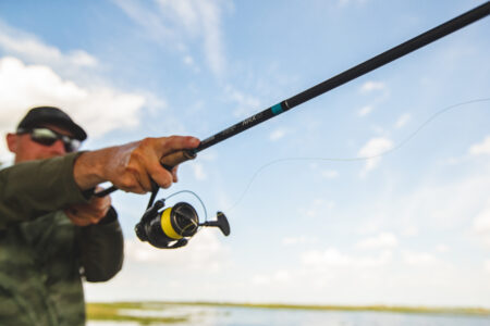 How to Cast a Spinning Reel Man casting fishing rod with spinning reel over open water on sunny day
