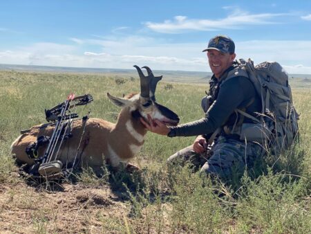 Hunter posing with harvested pronghorn antelope and crossbow on open grassland plains.