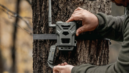 Person mounting a Spypoint Flex trail camera onto a tree in forest