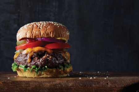 Juicy cheeseburger with tomato, red onion, and lettuce on sesame bun