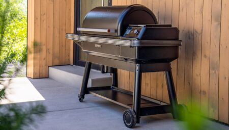 Black Traeger pellet grill on outdoor patio beside modern wood-paneled home