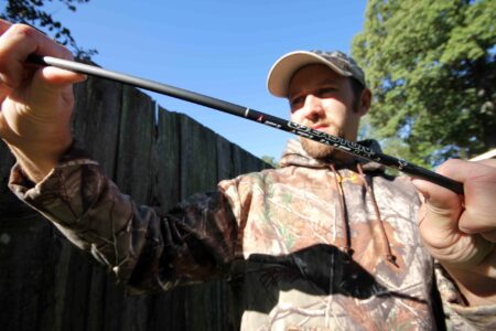Man in camo hoodie inspecting Easton carbon arrow shaft outdoors