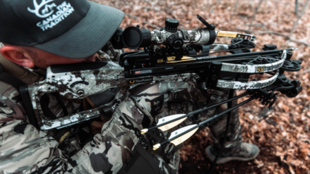 Best Crossbows for the Money of 2024 Hunter in camouflage aiming TenPoint crossbow with scope in woodland setting.