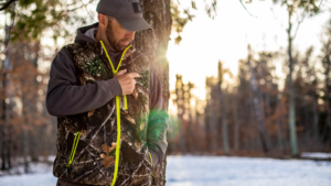 Man in camo hunting jacket adjusting safety harness in snowy forest