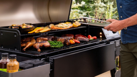 Man grilling assorted meats and vegetables on a large two-tier outdoor barbecue grill.