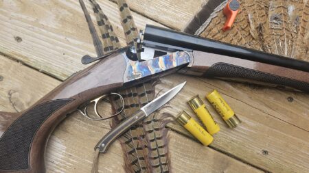 Side-by-side shotgun with hunting knife, yellow shotgun shells, and pheasant feathers