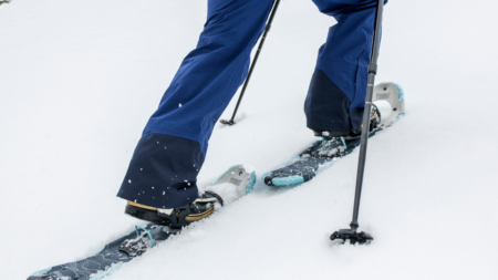 Person wearing blue ski pants snowshoeing in deep white snow with poles.