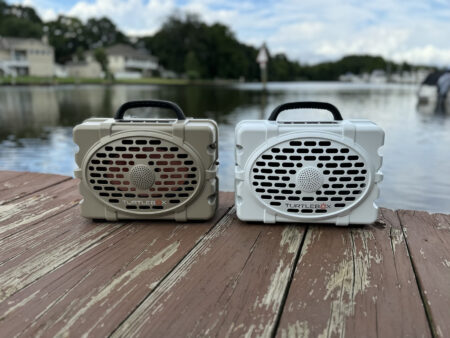 Two Turtlebox portable outdoor Bluetooth speakers on a wooden dock by water.