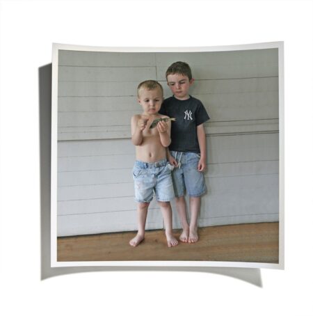 Two young boys standing barefoot holding a small fish on a porch.