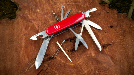 Red Victorinox Swiss Army multi-tool knife with all blades open on wood stump
