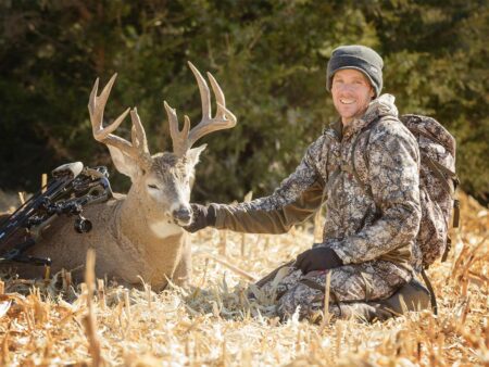 Bowhunter in camouflage posing with harvested whitetail buck deer in field