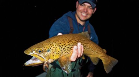 Smiling angler holding large brown trout caught during nighttime fishing trip