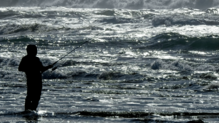 Best Waders for Surf Fishing in 2023 Silhouette of a person surf fishing in rough ocean waves at sunset
