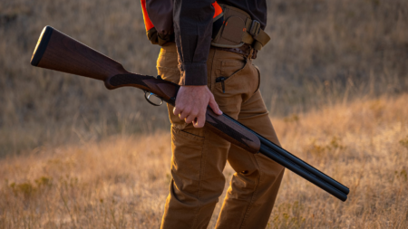 The Best Budget Shotguns at Every Price Point Hunter carrying an over-under shotgun in an open field at golden hour