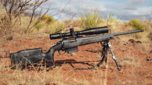 Bolt-action sniper rifle with scope and bipod resting on red desert ground