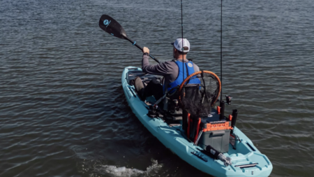 The Best Fishing Kayaks, Reviewed Man paddling a fishing kayak on calm water with fishing rods and gear