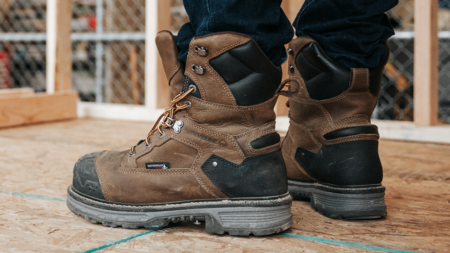 Brown waterproof Wolverine work boots worn on plywood construction site floor.