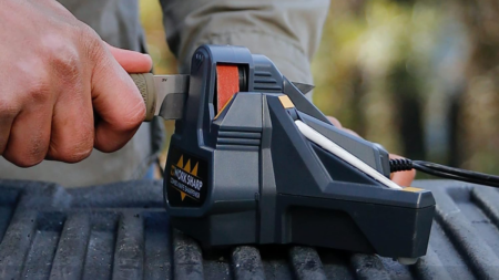 Person using Work Sharp electric knife sharpener on outdoor metal surface.