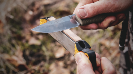 Person sharpening a Benchmade fixed blade knife with a portable field sharpener outdoors.