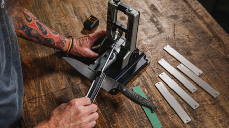 Tattooed person sharpening a knife using a professional electric knife sharpening machine.