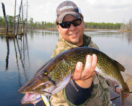 Smiling angler holding large walleye fish caught on lure at woodland lake