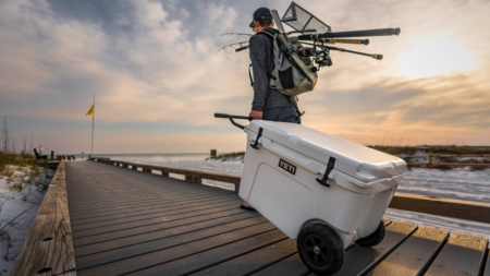 The 6 Best Fishing Coolers Angler pulling YETI cooler on wheels along beach boardwalk at sunset