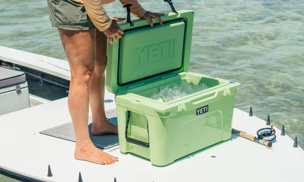 Yeti Is Secretly on Sale for Prime Day—Up to $90 Off Person opening green YETI Tundra cooler filled with ice on a fishing boat.