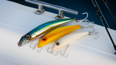 Three colorful fishing lures with treble hooks displayed on a white boat deck.