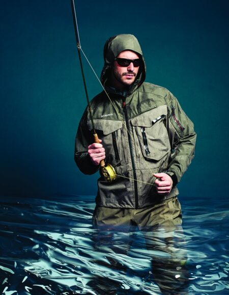 Man fly fishing in water wearing Simms hooded jacket and sunglasses