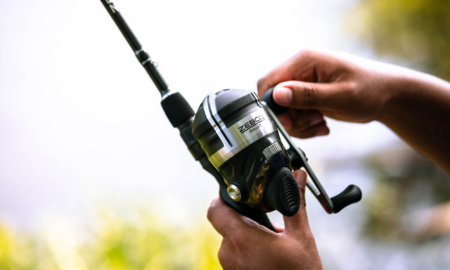 Zebco Rods and Reels Are Up to 50% Off Right Now Hands holding a Zebco Bullet spincast fishing reel attached to a rod outdoors.