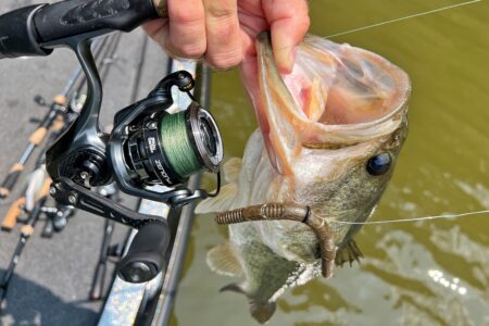 Abu Garcia Zenon MG-X Spinning Reel, Expert Tested Angler holds caught bass fish with plastic worm lure and spinning reel visible