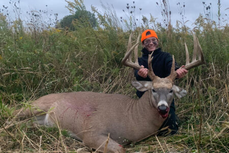 Thirteen-Year-Old Hunter Bags Giant 180-Inch Whitetail During Indiana Youth Hunt Young hunter in orange cap poses with harvested whitetail buck in field.