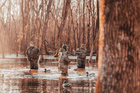 The Best Hunting Camos of 2024 Three duck hunters in camouflage wading through flooded forest with decoys.