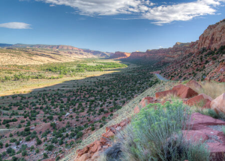 A New House Bill Would Erase Presidential Public Land Powers Enshrined by Theodore Roosevelt Red rock canyon valley with green vegetation and winding road under blue sky.