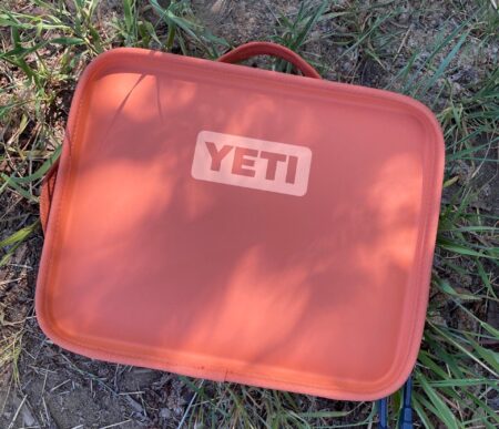 Orange YETI insulated lunch box bag lying on grass outdoors