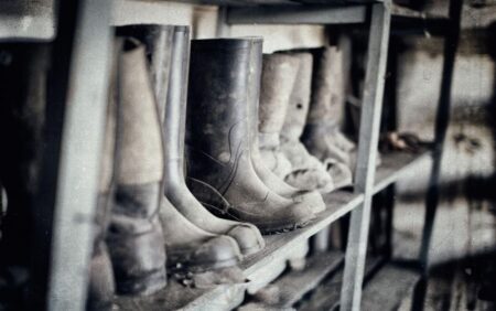 Worn rubber work boots lined up on metal shelves in storage